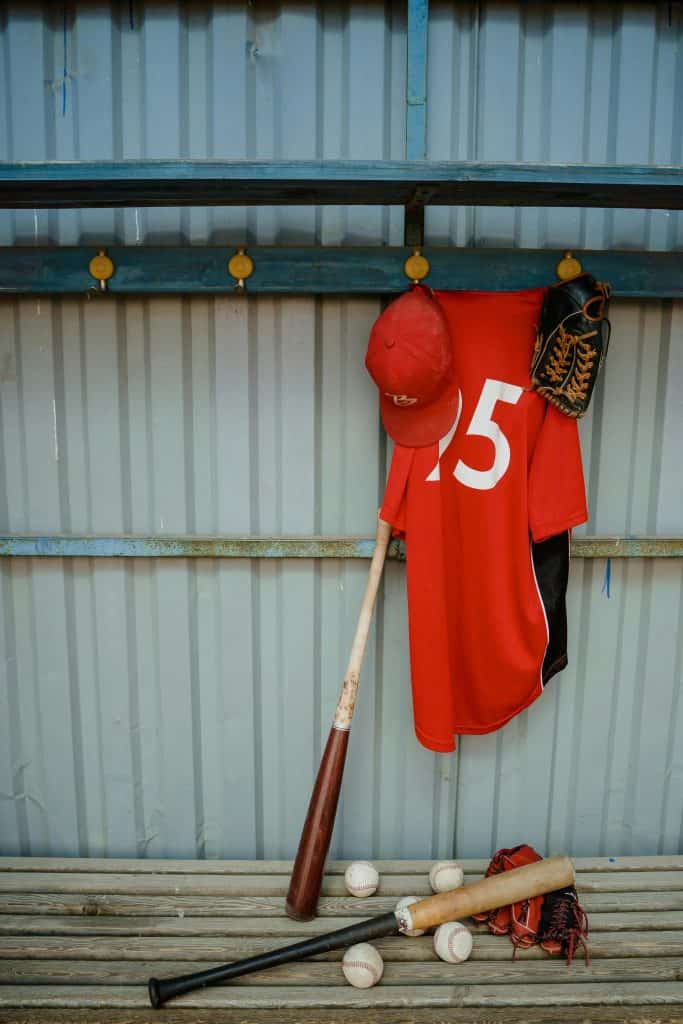 Baseball equipment including a jersey, bat, and balls in a dugout, representing the best snacks for baseball players during games.