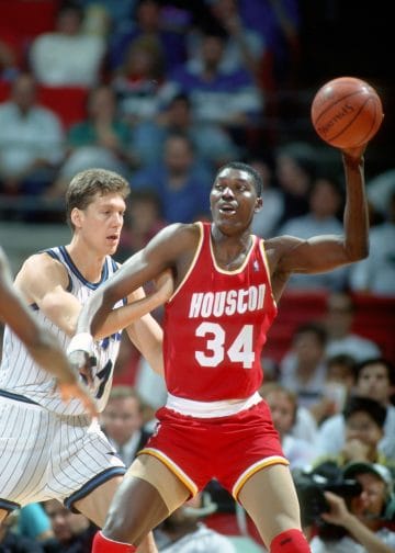 Hakeem Olajuwon of the Houston Rockets executing a post move against a defender during an NBA game, showcasing his iconic offensive skills against some bum who doesn't stand a chance.