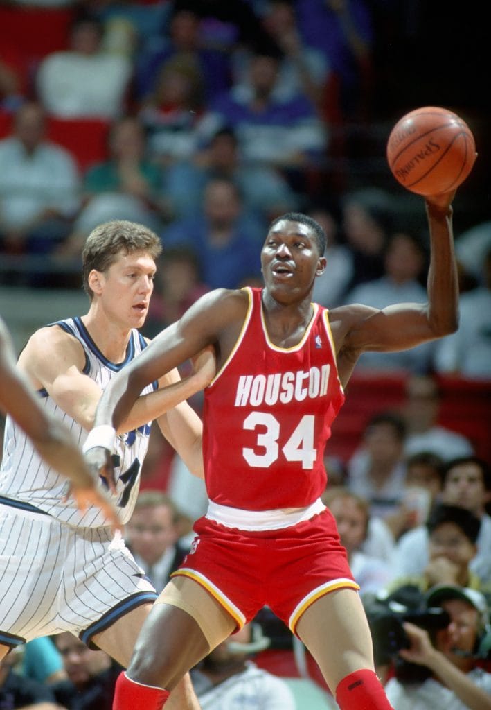Hakeem Olajuwon of the Houston Rockets executing a post move against a defender during an NBA game, showcasing his iconic offensive skills against some bum who doesn't stand a chance. 