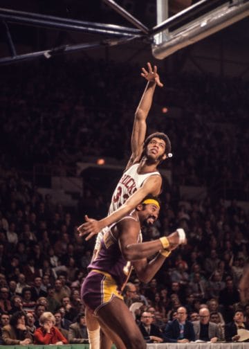 Kareem Abdul-Jabbar executing his iconic skyhook over Wilt Chamberlain during an intense NBA game, showcasing his legendary scoring ability.