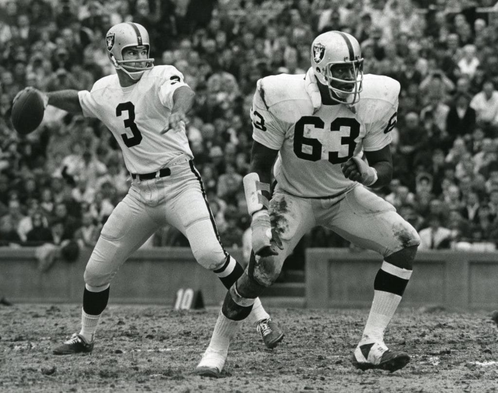 Raiders quarterback Daryle Lamonica prepares to throw while Gene Upshaw blocks during a game.