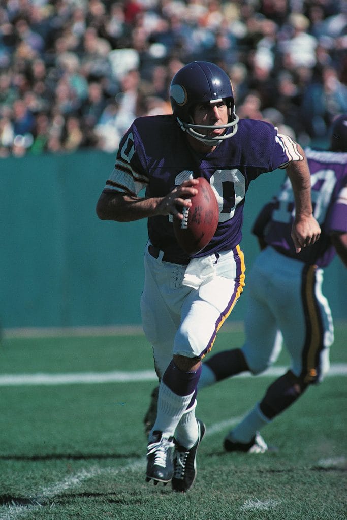 Fran Tarkenton of the Minnesota Vikings runs with the football during a game, evading defenders.