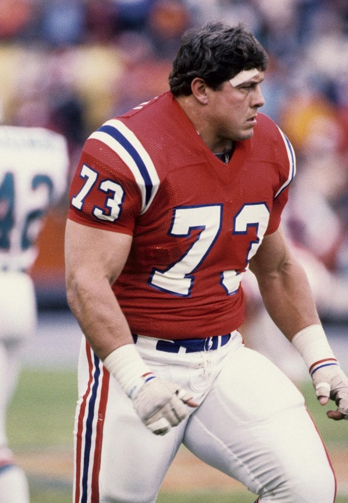 John Hannah of the New England Patriots walks on the field in a red jersey.