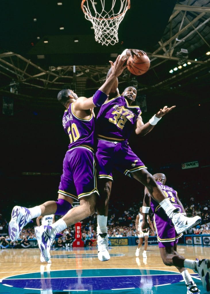 Karl Malone of the Utah Jazz jumps to secure a rebound during a game with teammate Bryon Russell nearby.