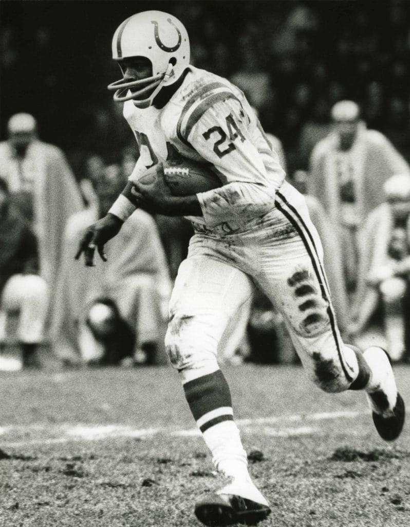 Lenny Moore of the Baltimore Colts running with the football during a game in a muddy field.