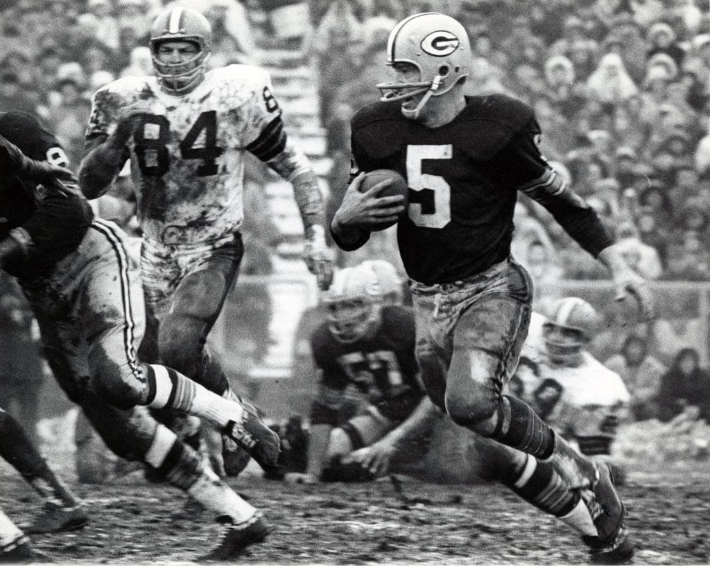 Paul Hornung of the Green Bay Packers running the ball on a muddy field during a game, evading defenders.