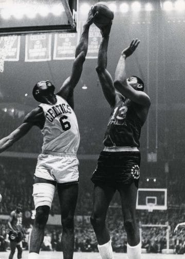 Bill Russell of the Boston Celtics and Wilt Chamberlain of the Philadelphia 76ers leap for the ball under the basket during a classic NBA matchup.