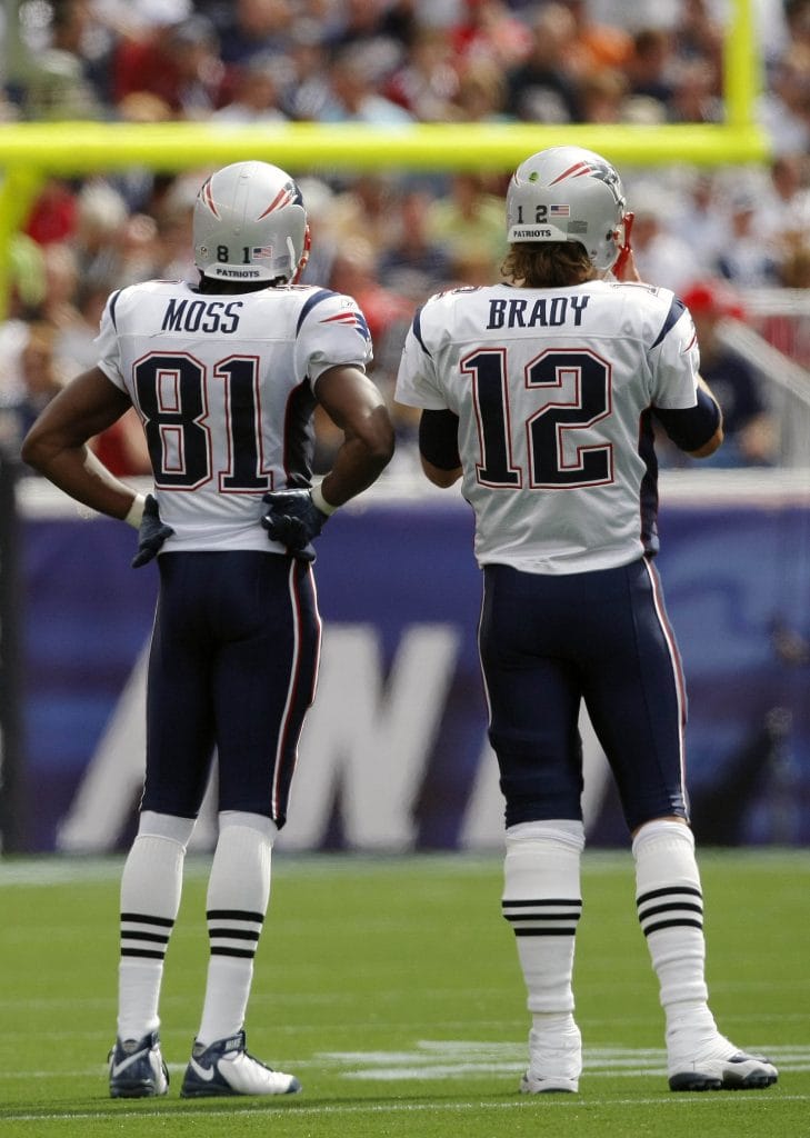 Tom Brady and Randy Moss of the New England Patriots discussing strategy on the field during a game representing 2 of Top 10 New England Patriots of All Time.