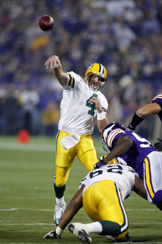 Brett Favre of the Green Bay Packers throwing a pass against the Minnesota Vikings during an NFL game, wearing a white jersey.