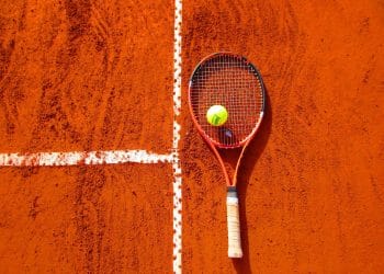 Tennis racket and ball on a clay court, symbolizing the skill and legacy of the greatest tennis players of all time.