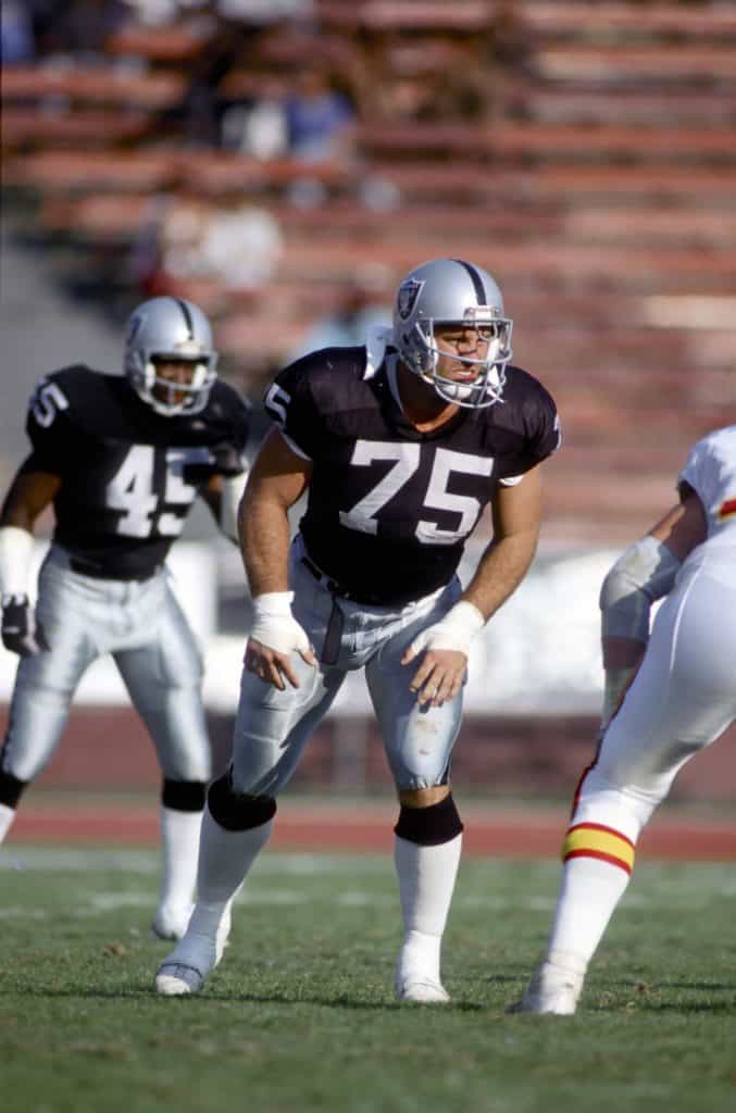 Los Angeles Raiders defensive end Howie Long preparing for a play, focused and ready on the field.