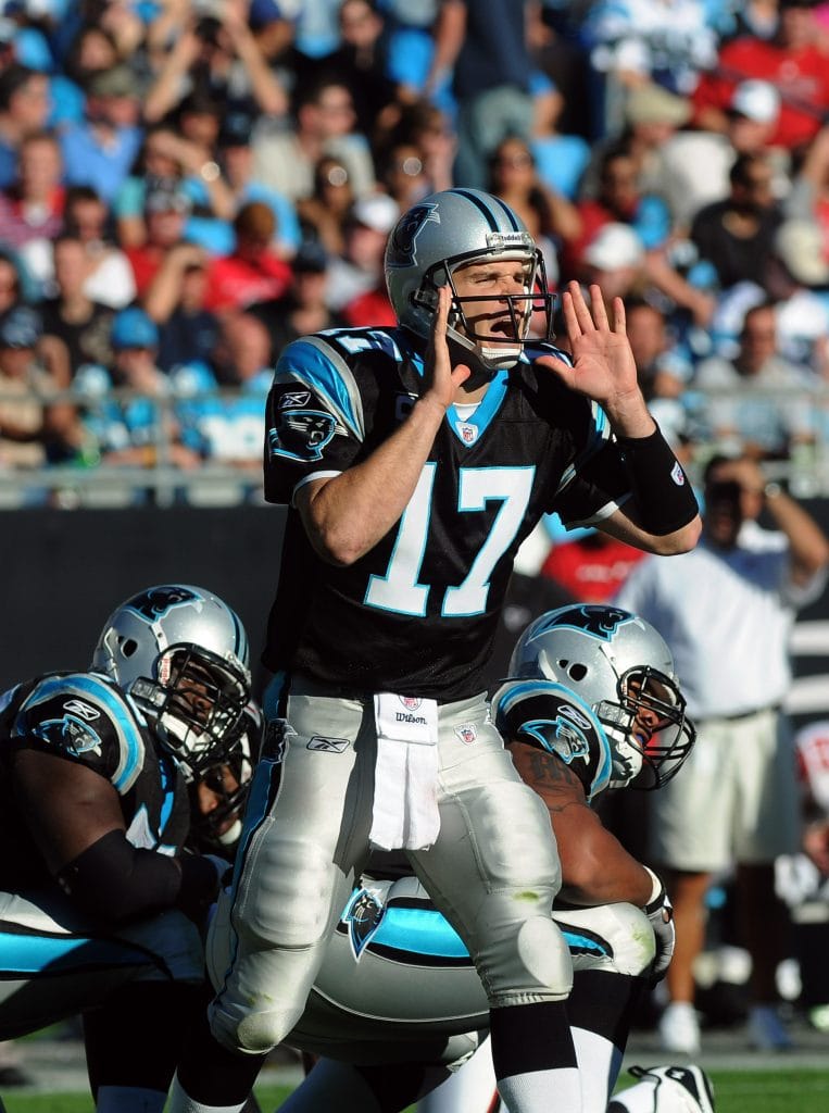 Carolina Panthers quarterback Jake Delhomme shouting out instructions to his team during a game, standing behind his offensive line.