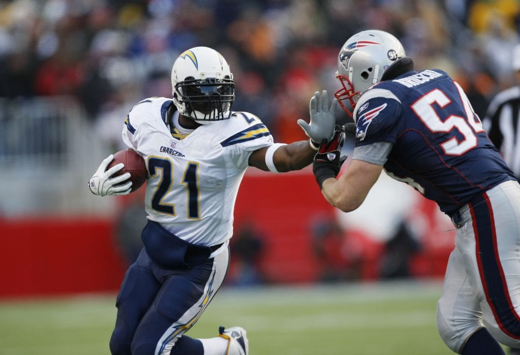LaDainian Tomlinson of the San Diego Chargers, wearing number 21, using a stiff arm against a New England Patriots defender during a game.