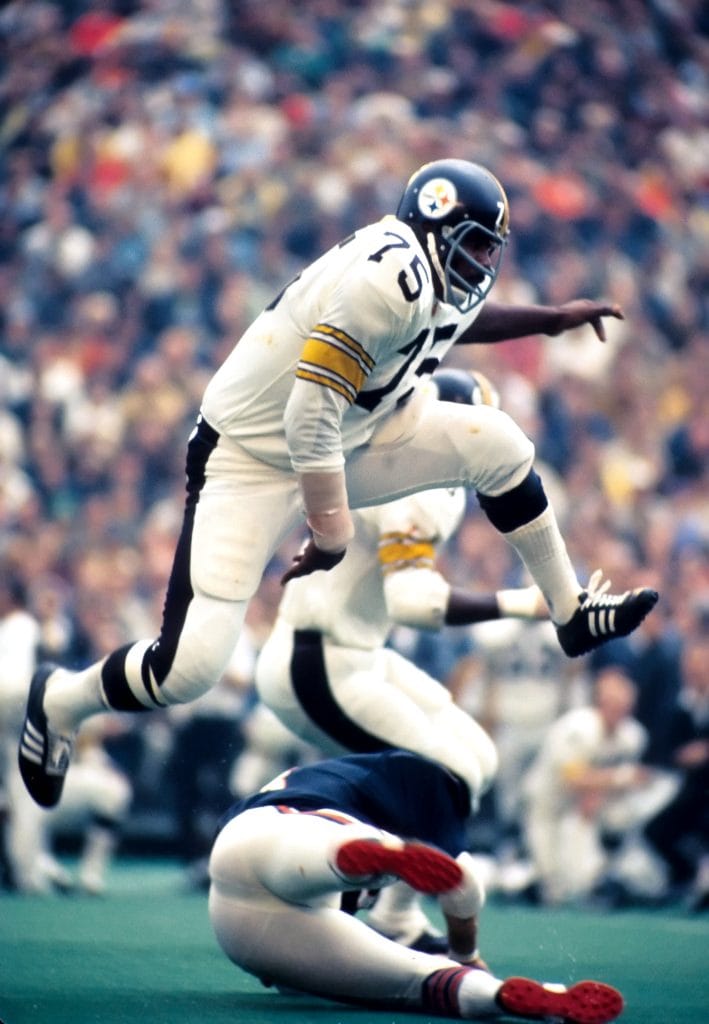 Mean Joe Greene, Pittsburgh Steelers defensive tackle, wearing number 75, leaping over a player during a game.