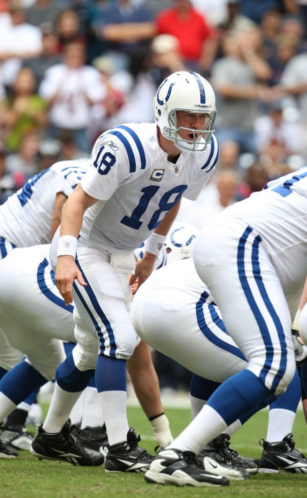 Peyton Manning in a white Indianapolis Colts uniform, preparing to snap the ball during a game.