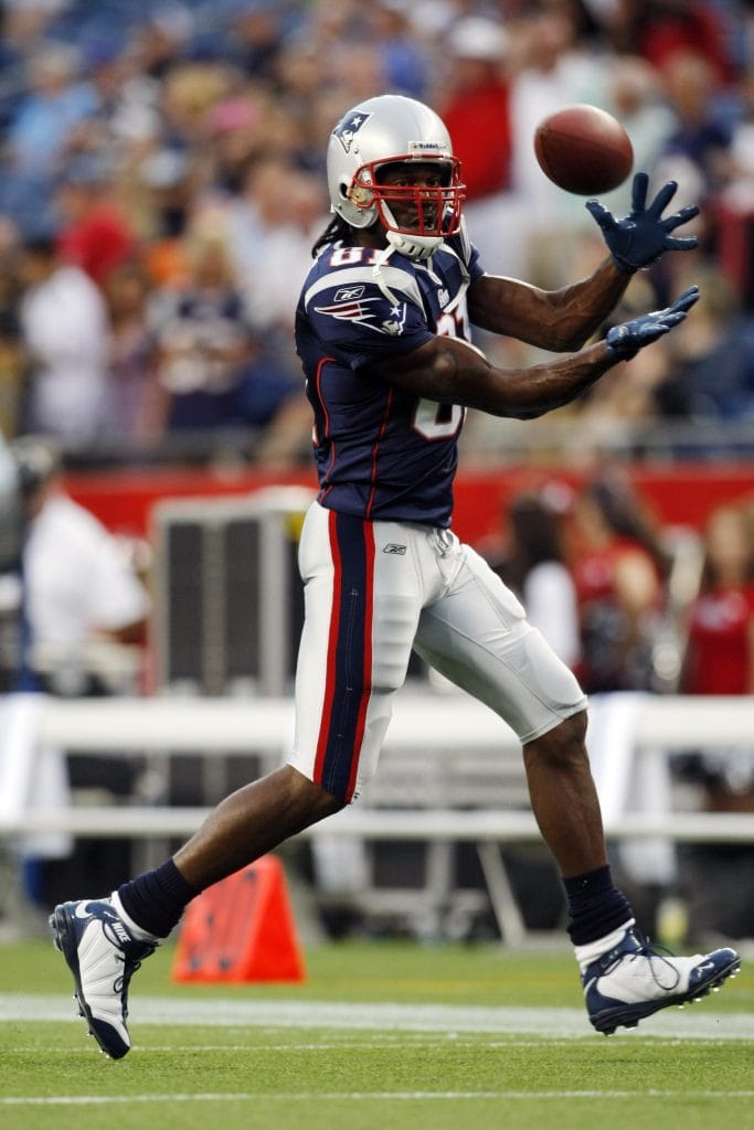 Randy Moss of the New England Patriots extending his arms to catch a football during a game.