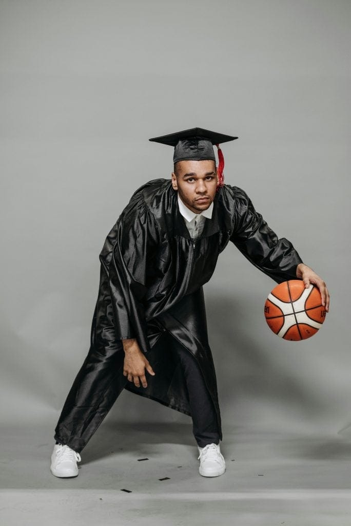 Athlete in graduation attire holding a basketball, representing the top 5 smartest athletes who excel in both academics and sports.