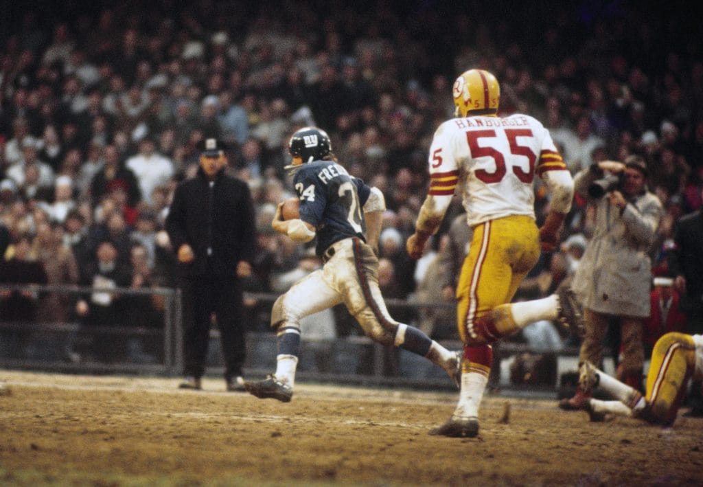 New York Giants running back Tucker Frederickson running down the field with the football, pursued by a Washington linebacker.
