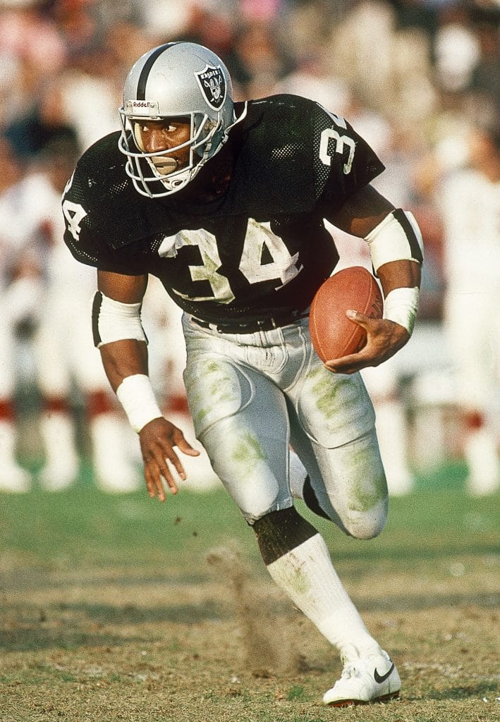 Bo Jackson of the Los Angeles Raiders sprinting with the football in open field during a game.