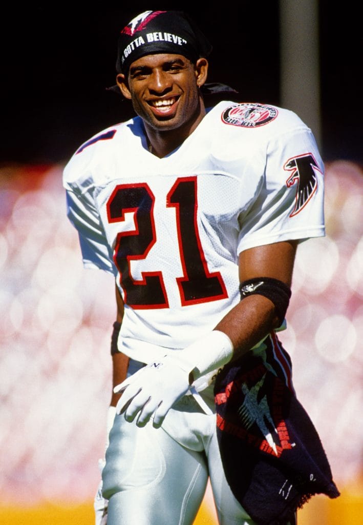 Deion Sanders smiling in his Atlanta Falcons uniform during an NFL game.