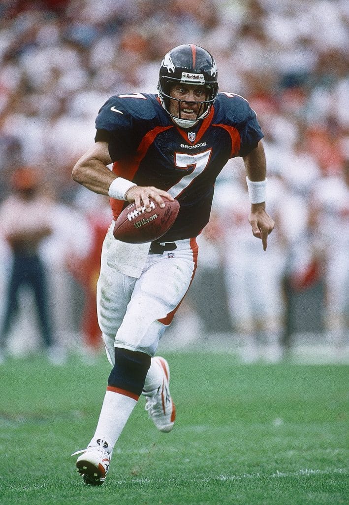 John Elway in action, running with the football for the Denver Broncos.