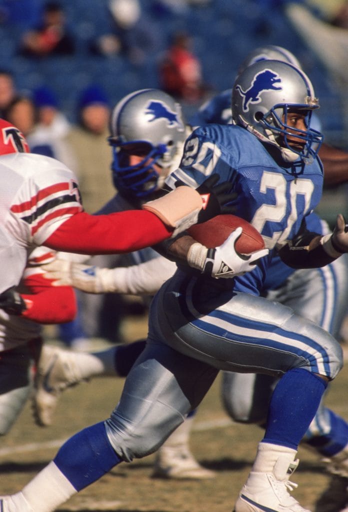 Barry Sanders evading defenders while carrying the football for the Detroit Lions during a game.