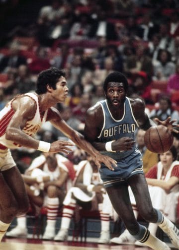 Bob McAdoo, legendary Buffalo Braves center, dribbling past a defender during an NBA game.