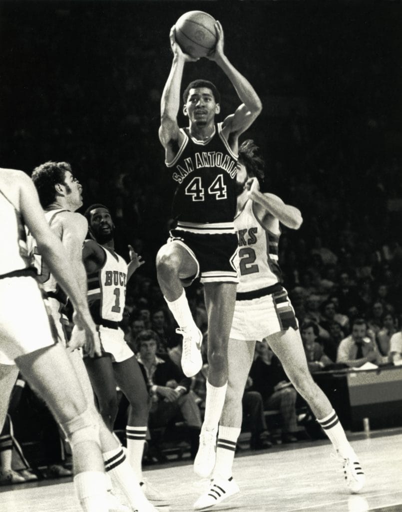 George Gervin executing a jump shot in his San Antonio Spurs uniform, surrounded by Milwaukee Bucks defenders.