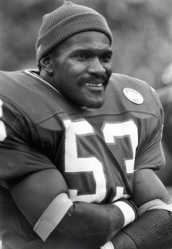 New York Giants linebacker Harry Carson smiling on the sideline during a game.