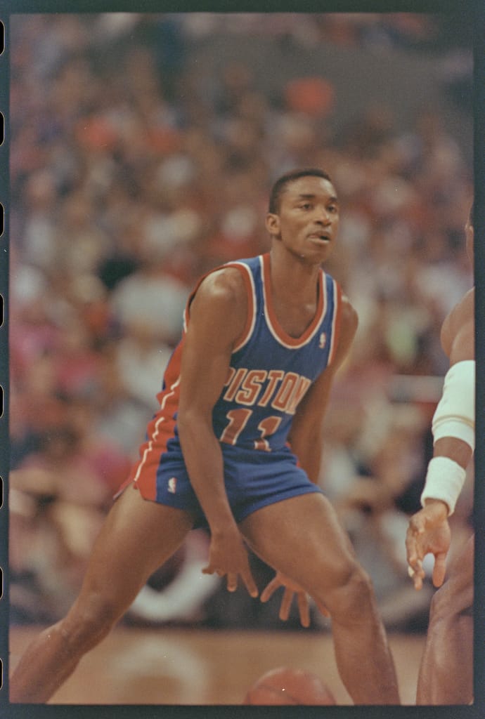 Detroit Pistons' Isiah Thomas in a poised offensive stance, holding the basketball with intensity and ready to make a play against the defense.