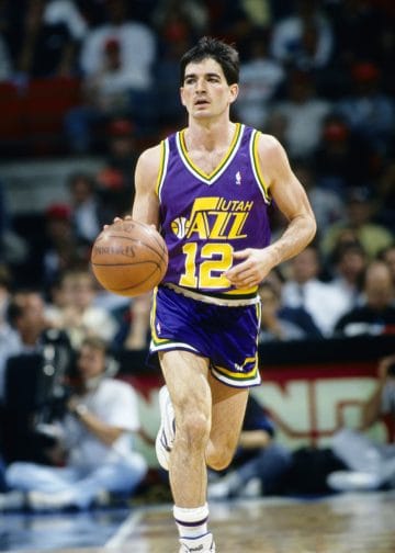 John Stockton dribbling the ball for the Utah Jazz in a game, showcasing his legendary playmaking and court vision as one of the greatest point guards in NBA history.