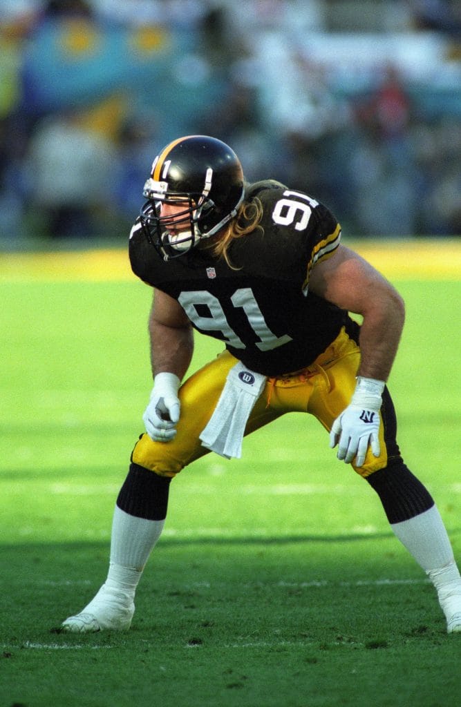 Kevin Greene in his Pittsburgh Steelers uniform, crouched in a ready stance during a game.