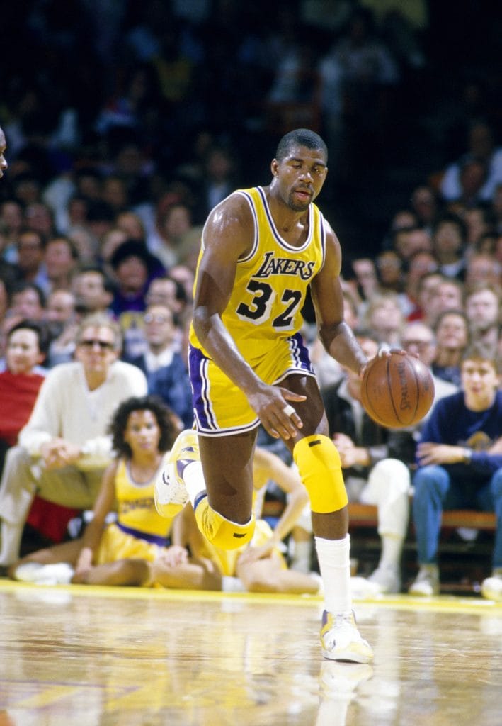 Magic Johnson dribbling the ball up the court during a Los Angeles Lakers game, showcasing his court vision and signature style.