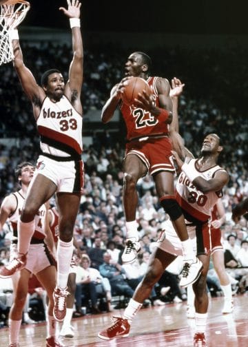 Michael Jordan executing an acrobatic layup against the Portland Trail Blazers, showcasing his agility and finesse on the court.