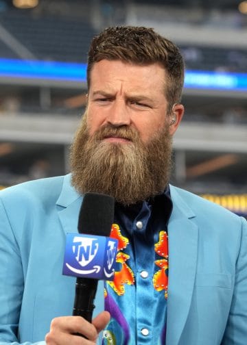 Ryan Fitzpatrick, known for his Harvard background, speaks during an NFL broadcast wearing a colorful shirt and suit jacket.