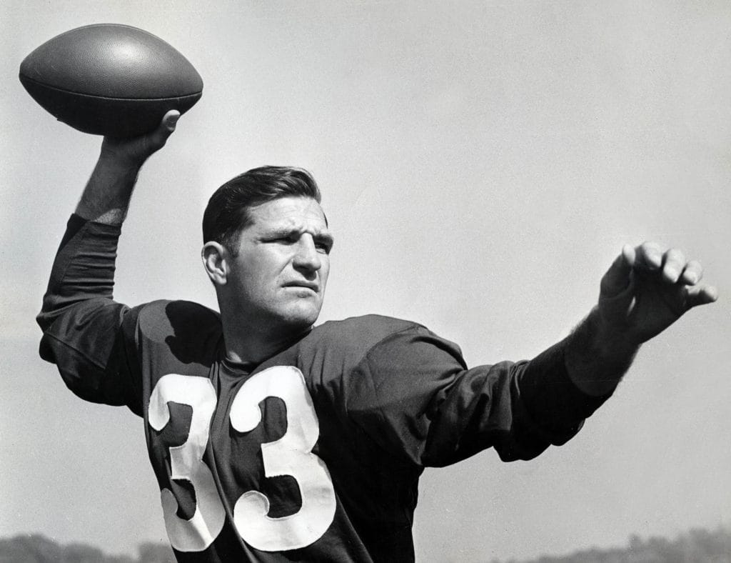 Sammy Baugh in a classic Washington Redskins uniform, preparing to throw a pass, showcasing his legacy as one of the Top 10 Washington Commanders of All Time.