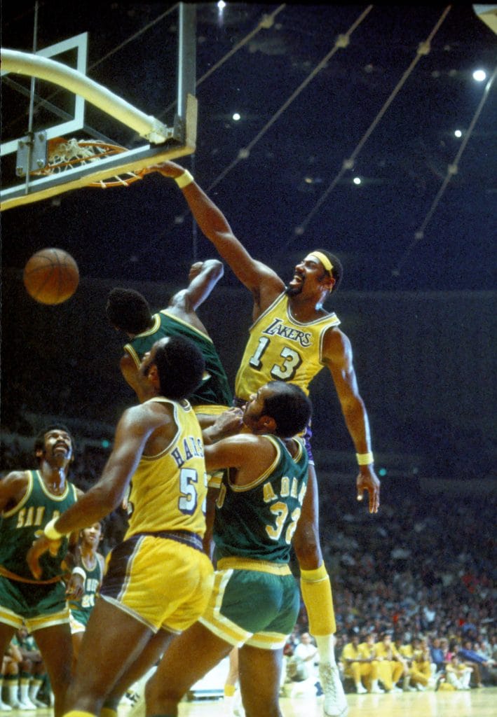 Wilt Chamberlain executing a powerful dunk in a Lakers jersey, surrounded by defenders, exemplifying his dominance on the court.