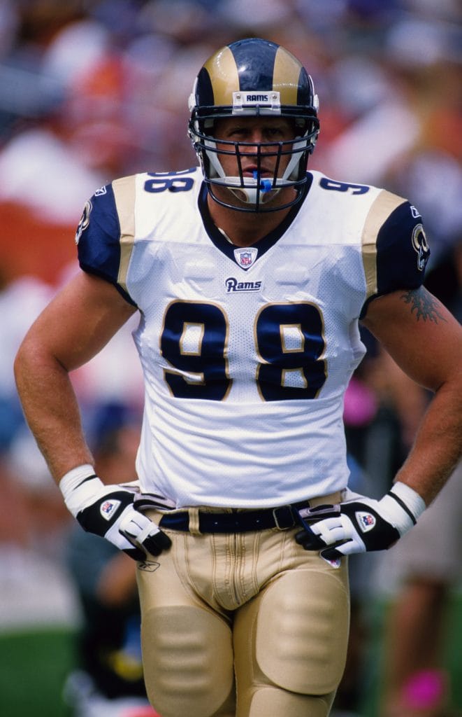 Grant Wistrom, a famous white NFL player, stands ready on the field while representing the St. Louis Rams as a defensive end.
