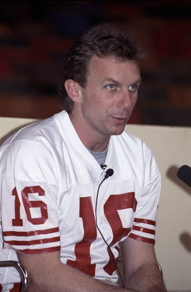 Joe Montana in a 49ers jersey during a press conference, highlighting his status as one of the best white NFL players of all time and a famous white football player.