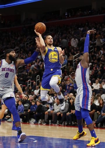 Golden State Warriors guard Stephen Curry driving through defenders for a layup against the Detroit Pistons, showcasing why he belongs among the Top 10 Point Guards of All Time.
