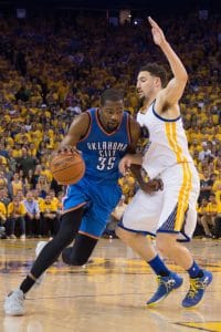 Kevin Durant driving past future teammate Klay Thompson in a blue OKC jersey. 