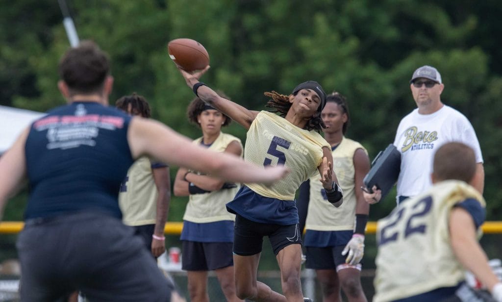 Quarterback launches a pass during 7v7 football competition with teammates looking on.