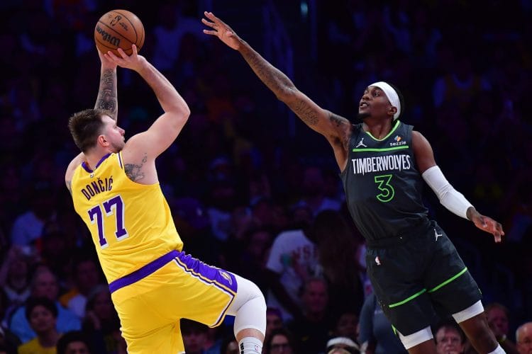 White basketball player Luka Doncic shooting a fadeaway jumper against the Timberwolves in a Lakers uniform. 