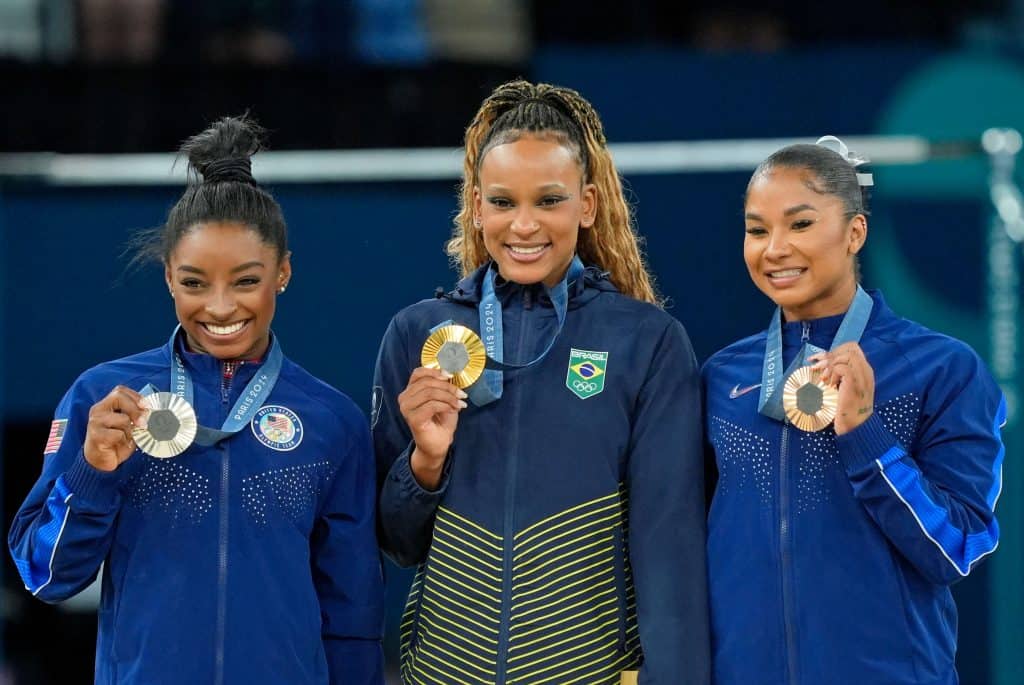 Rebeca Andrade, Simone Biles, and Shilese Jones smiling on the podium after the balance beam final during the Artistic Gymnastics Olympics