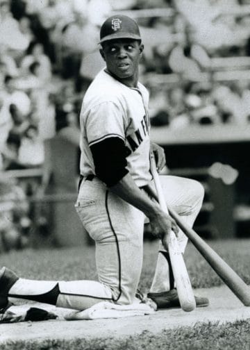 Black baseball icon Willie Mays kneeling with two bats during his time with the San Francisco Giants. 